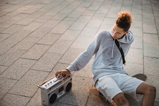Young man enjoys music on boombox while sitting on skateboard in urban setting.