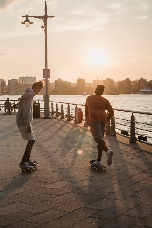 Faceless sporty men skating on embankment at sunset