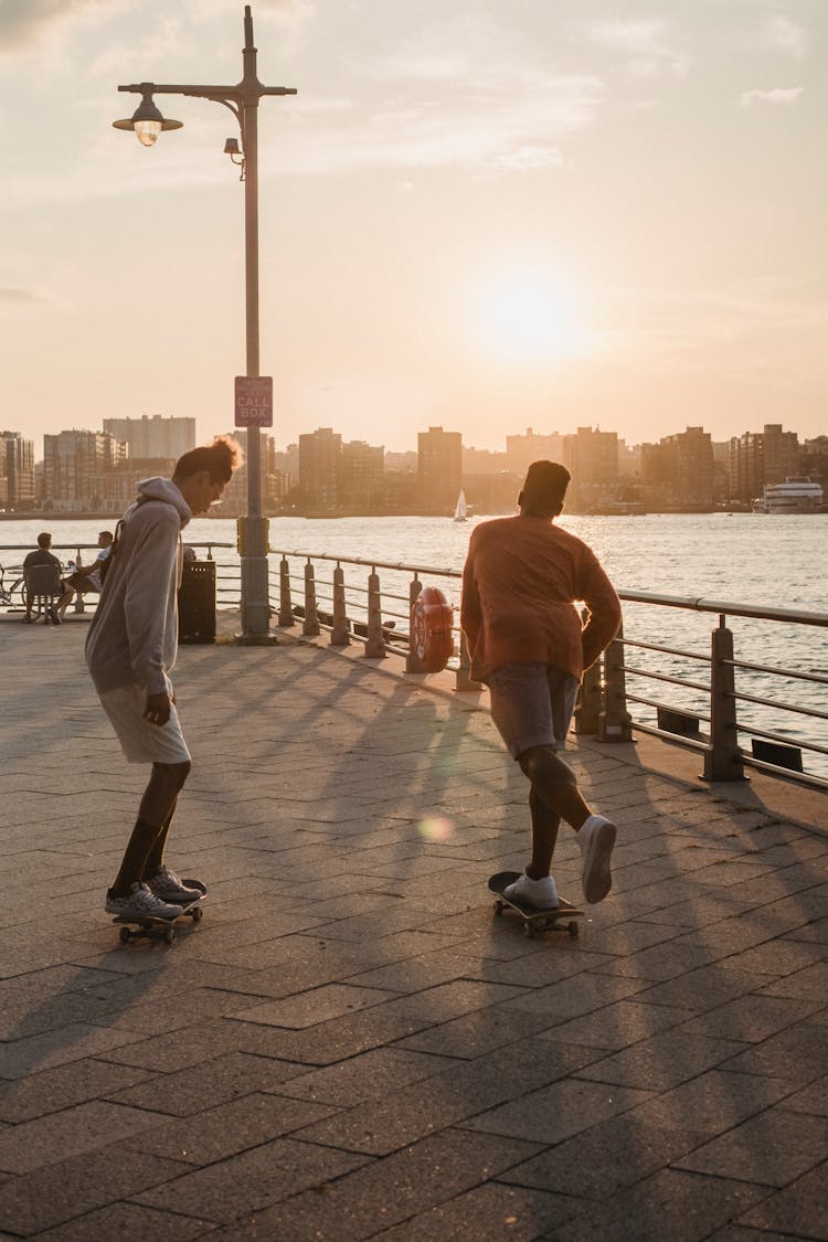 Faceless Sporty Men Skating On Embankment At Sunset