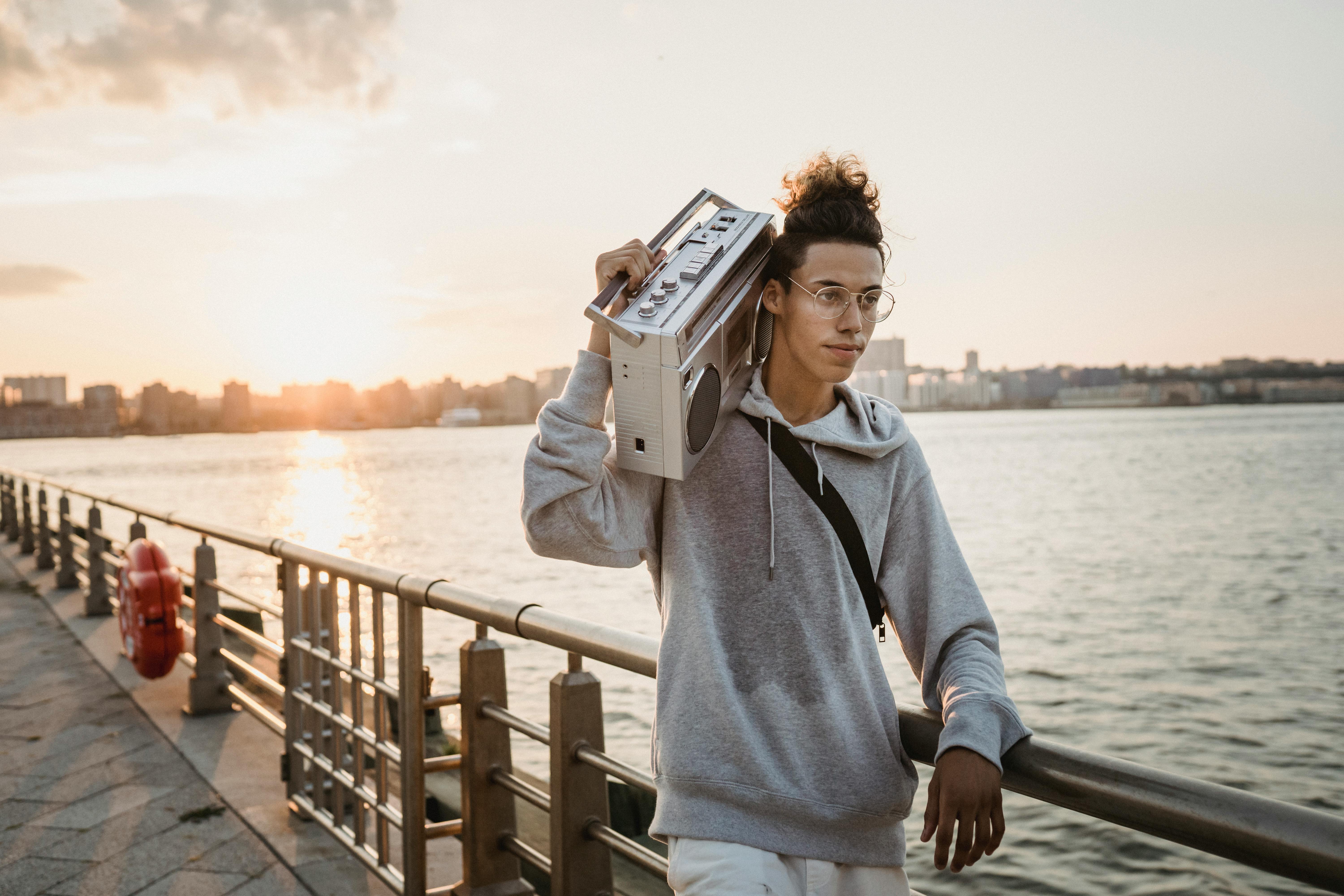 positive ethnic man carrying boombox on shoulder on embankment