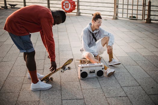 Full length happy laughing diverse male skaters spending evening on city waterfront and listening to favorite music via tape recorder