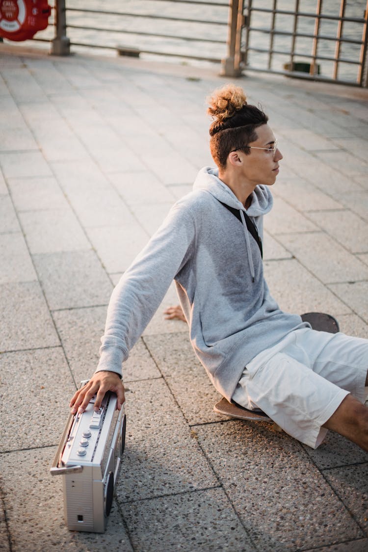 Ethnic Man Sitting On Skateboard With Retro Tape Recorder