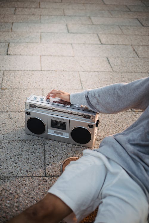 Crop anonymous man listening to music with boombox on street
