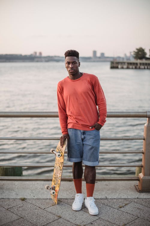 Sporty young black guy chilling on pier after riding skateboard