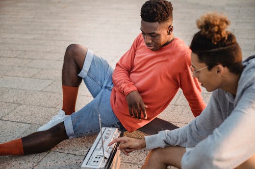 Free Side view of stylish young multiracial male friends in casual outfits relaxing on street at sunset and listening to music with vintage boombox Stock Photo