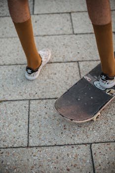 From above of crop unrecognizable slim male teenager in stylish sneakers and socks riding skateboard on paved street