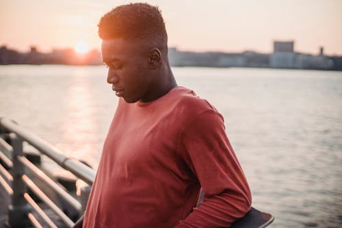 Réfléchi Jeune Homme Noir Reposant Sur La Jetée Sous Le Ciel Du Coucher Du Soleil