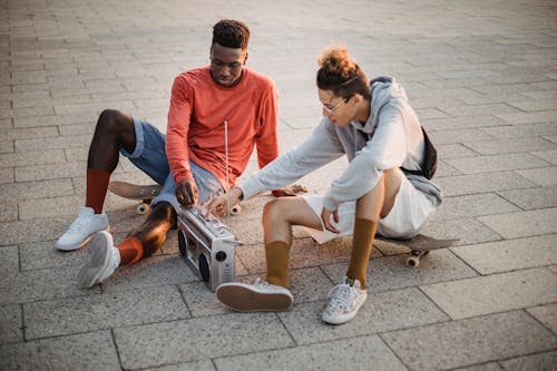 Free High angle of multiethnic friends listening to music on old fashioned portable sound system sitting on skateboards Stock Photo