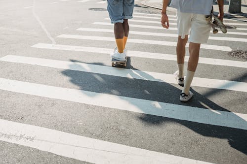 Back view of anonymous black man riding skateboard while crossing road with friend while spending pastime together