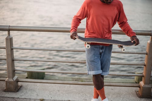 Black man in casual wear with skateboard on promenade