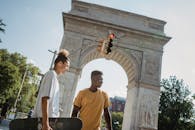 From below of multiethnic male skateboarders standing against aged stone Triumphal Arch in USA