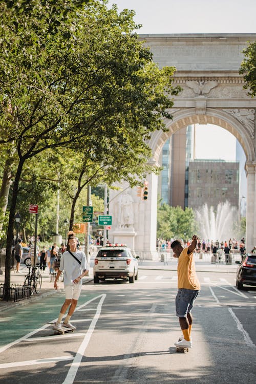 Full body of active carefree diverse friends riding skateboards together on asphalt road against USA landmark Triumphal Arch