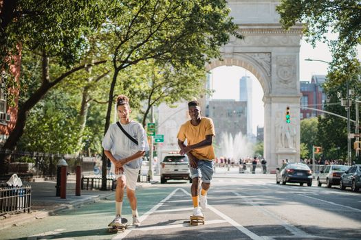 Full body of serious multiethnic male skateboarders riding skateboards along road against Triumphal Arch in New York