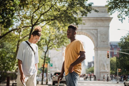 Stylish young multiethnic male friends in casual clothes standing on street near Washington Square Arch on sunny day in New York