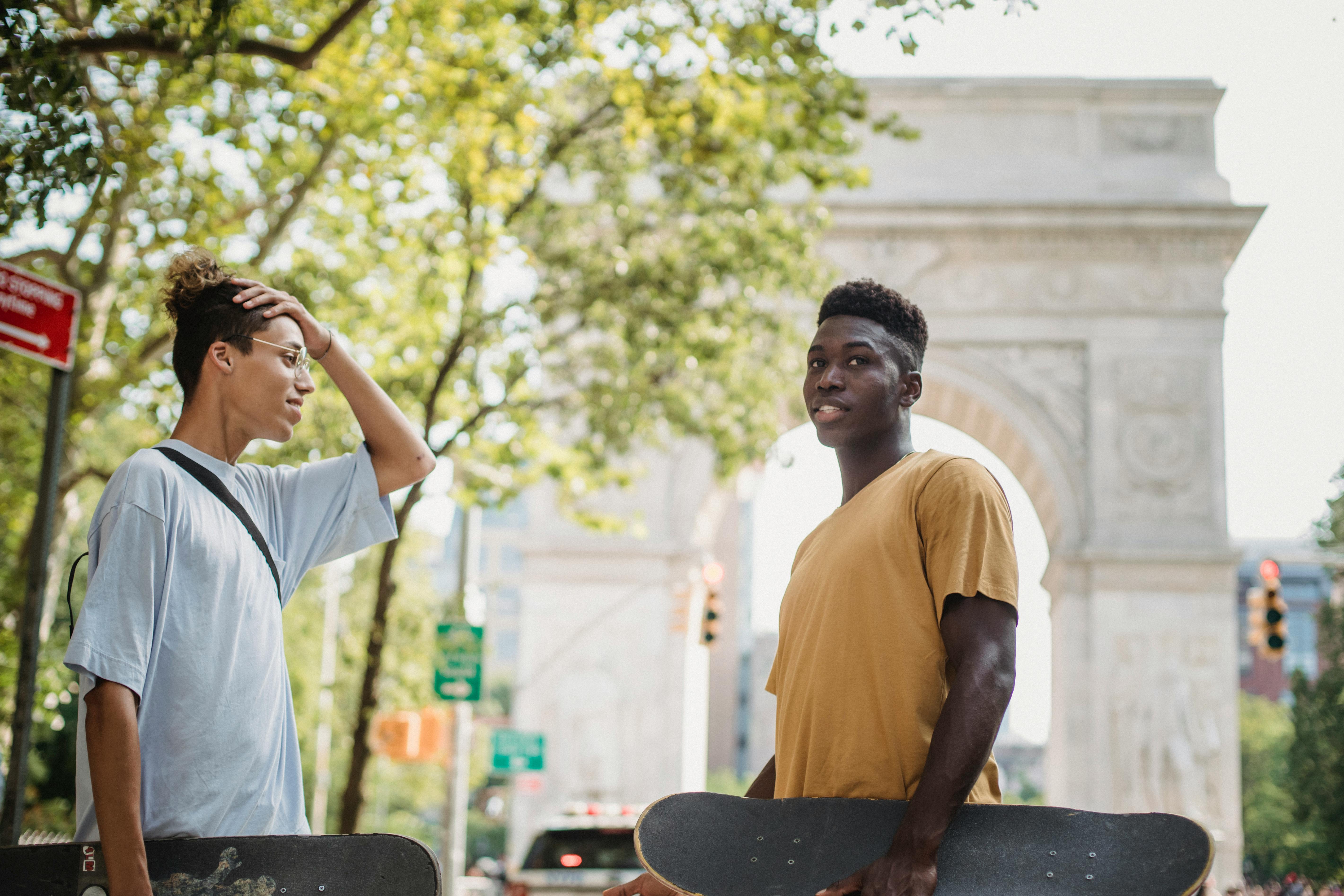 positive young multiracial guy standing together on street with skateboards after training