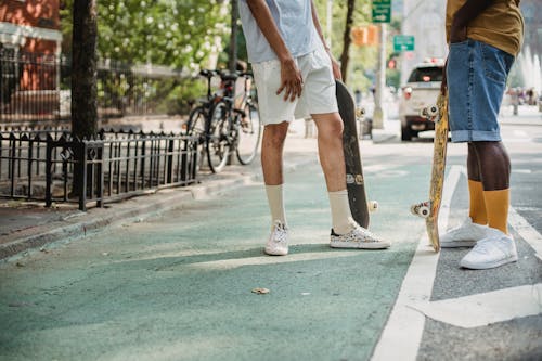 Anonymous trendy male friends chatting on street after skateboarding