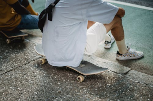 Unrecognizable diverse male skaters sitting on boards at roadside