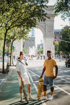 Full body of fashionable young multiracial guys with skateboards in stylish outfits standing on city street and looking at camera near Washington Square Arch on sunny day by Budgeron Bach