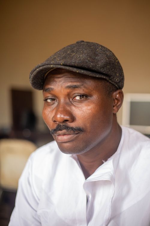 Free Serious African American man with mustache wearing white outfit and cap looking at camera while sitting in room with blurred interior Stock Photo