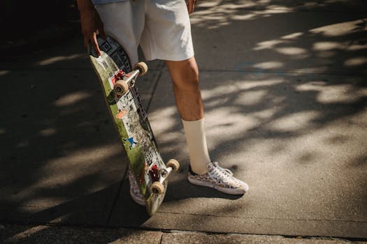 A young skater holding a skateboard in a sunlit urban setting, showcasing street style fashion.