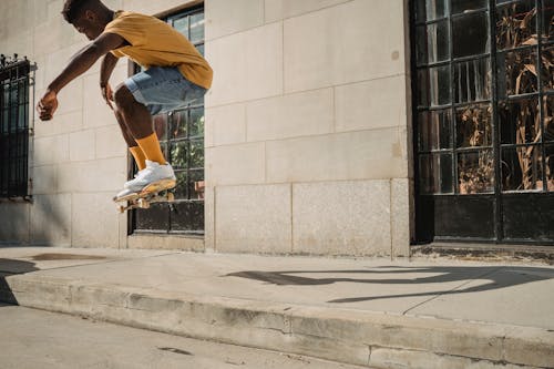Crop faceless black man jumping on skateboard on street
