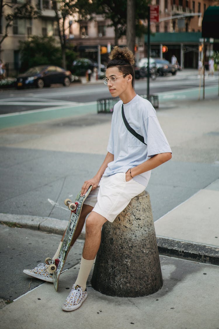 Positive Ethnic Male Skater Sitting On Street Bollard