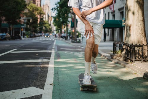 Crop faceless skater riding skateboard along sunny street