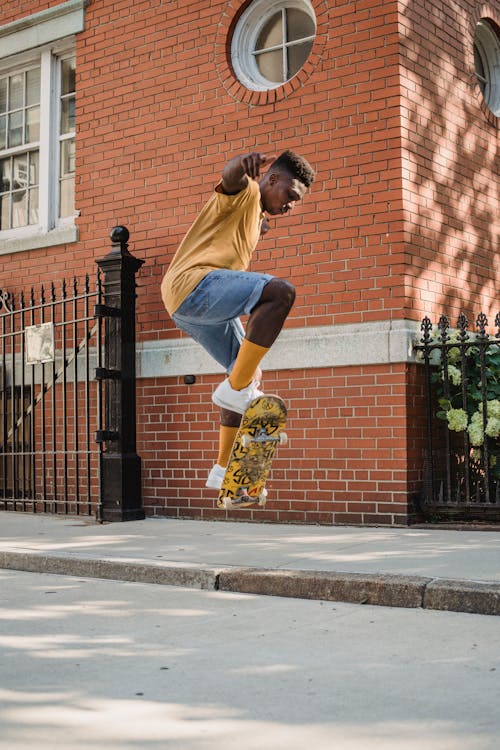 Free Side full length fit African American male skater in casual summer wear jumping on skateboard on street sidewalk on sunny day Stock Photo