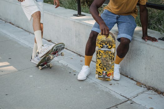 Crop anonymous multiethnic male skaters in summer shorts skating together on roadside in sunny city