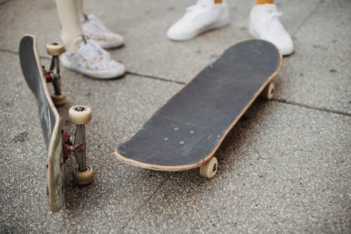 Crop faceless skaters standing on street near skateboards