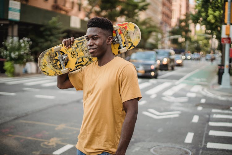 Cheerful Black Man Carrying Skateboard On Shoulder On Street