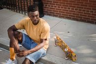 Confident young black male skater resting on sidewalk near brick building