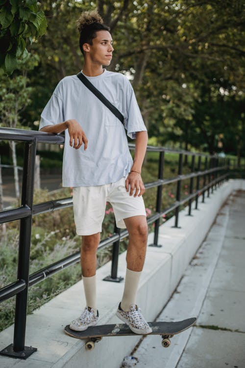 Jinete Masculino Joven Serio De Pie En La Cola Del Monopatín En El Parque De La Ciudad