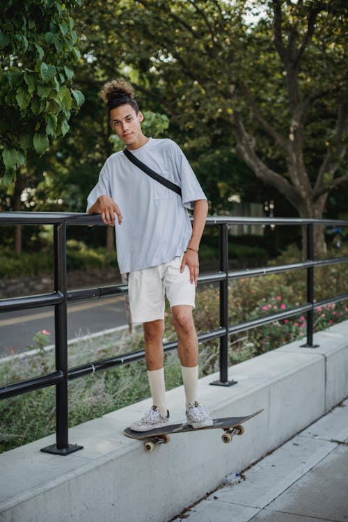 Grave Joven Skater Masculino étnico De Pie A Bordo Y Apoyado En La Valla Metálica