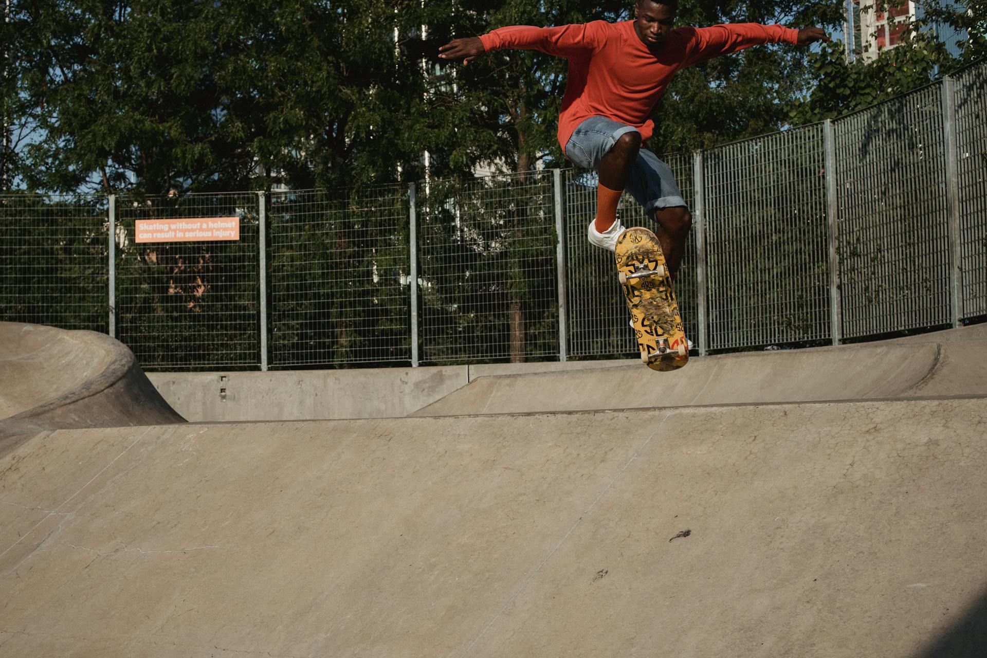 Crop African American male skateboarder performing dangerous ollie stunt on concrete ramp in skate park located in city on sunny day