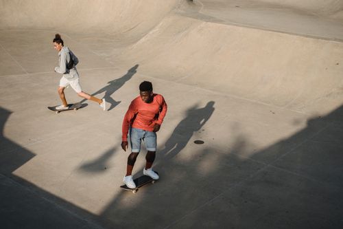 Free From above of man diverse friends accelerating for performing extreme stunt on skateboard during training on modern ramp in skate park Stock Photo