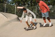 Young men in casual outfit skateboarding on ground of ramp