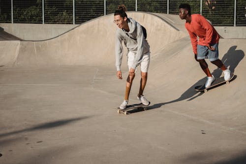 Free Happy young guy and African American friend getting ready to perform trick on skateboard on asphalt ramp in skate park on sunny weather Stock Photo