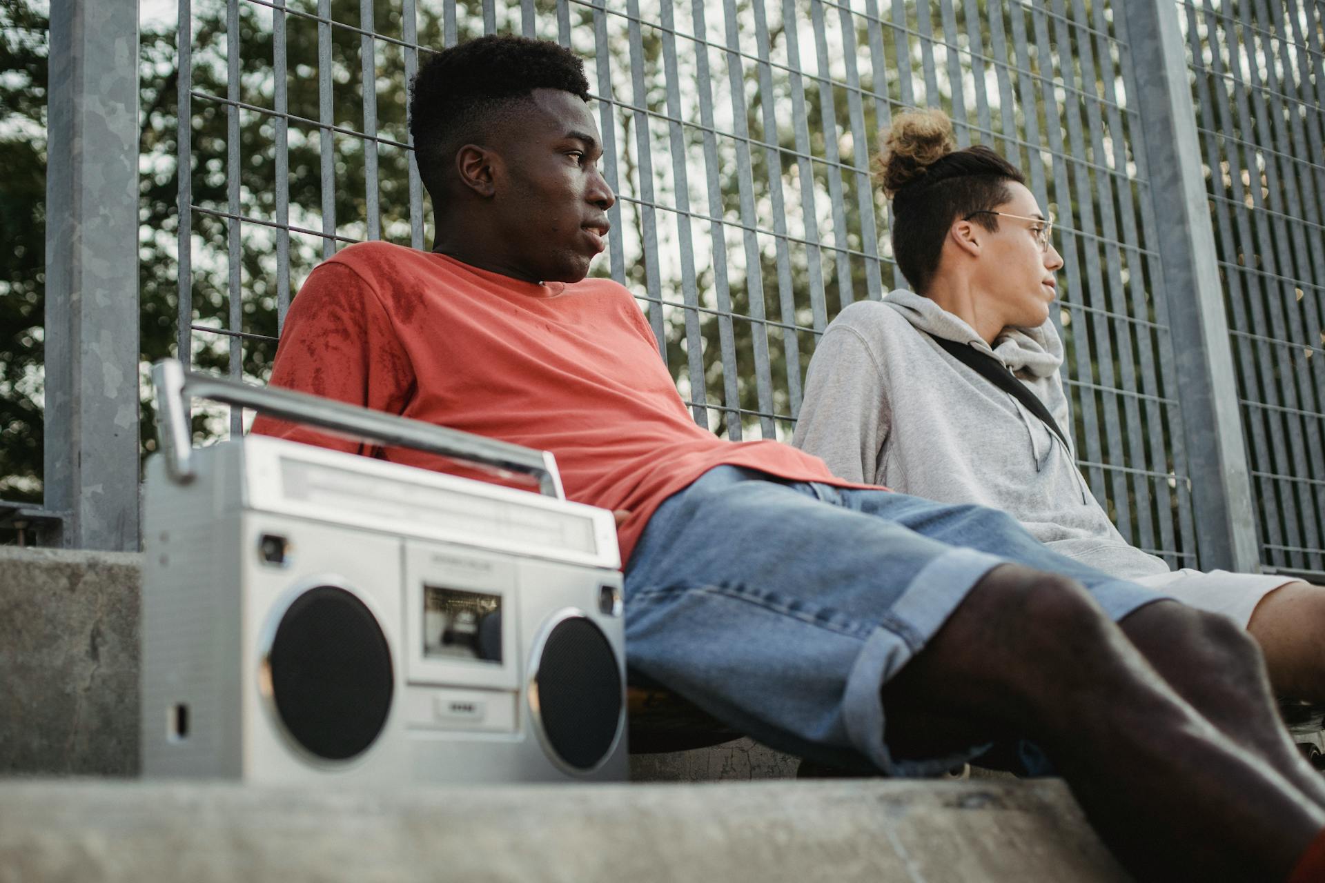 Diverse friends with boombox resting near fence in park