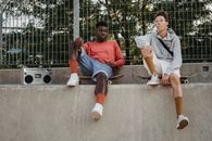 From below of serious multiracial young friends resting on skateboards and listening to music on vintage boombox in skate park