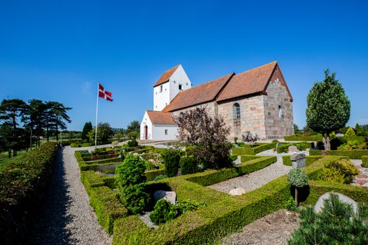 Beautiful historic church in Denmark surrounded by a well-maintained garden on a sunny day.