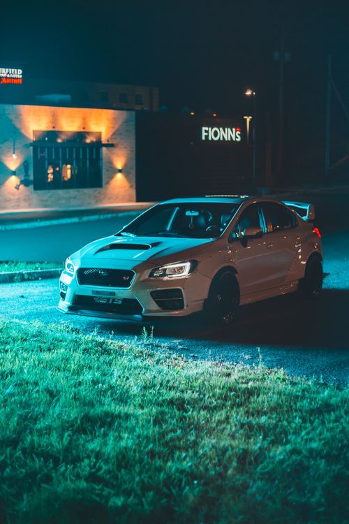 Free Bright modern automobile parked near green lawn and building with glowing lights late at night Stock Photo