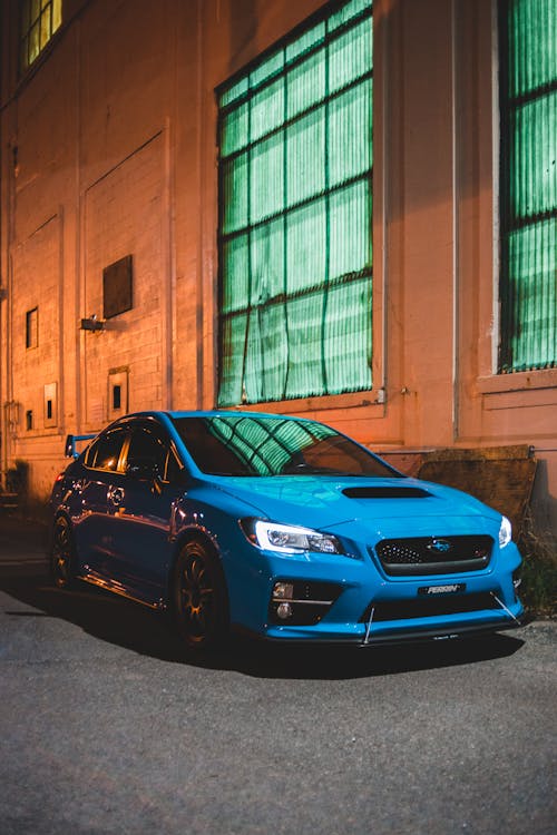 Contemporary blue automobile parked near aged house with large windows in late evening