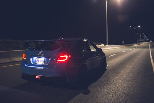 A sleek blue car drives under streetlights on a quiet city road at night, showcasing modern design and speed.