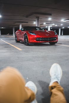 A red sports car parked in a dimly lit garage with a relaxed man in the foreground.