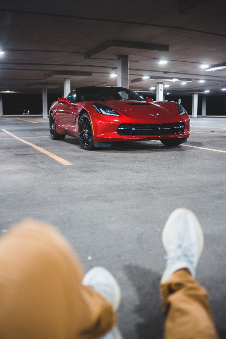 Young Man Sitting On Parking Lot With Modern Car