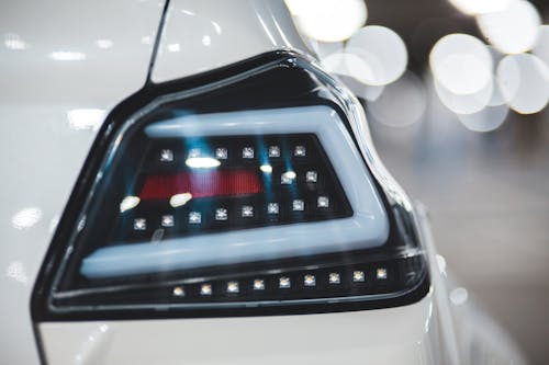 Closeup of shiny white colored vehicle with stylish headlight against blurred lights of parking lot