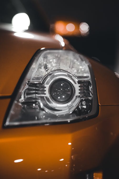 Closeup of shiny glass light at front of motor vehicle against blurred lights of lamp