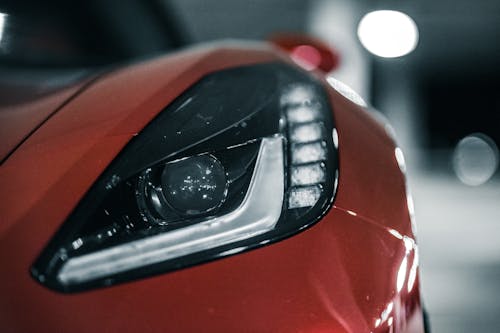 Closeup of elegant shiny headlight of new red expensive sport car parked at car park