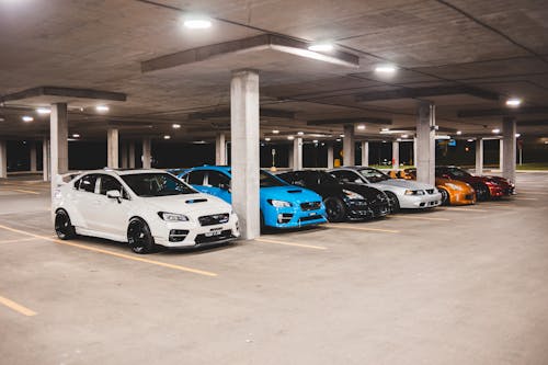 Bright new expensive automobiles placed on parking lot under concrete roof with bright lights